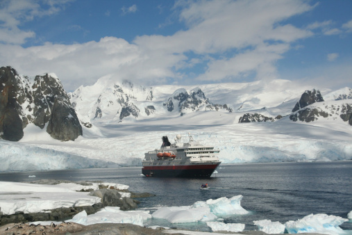 Sunset in Antarctica. Large coastal iceberg drifting under moody dramatic sunset skyscape in front of Antarctic Mountain Range and Glacier. Antarctic Ocean, Antarctica.