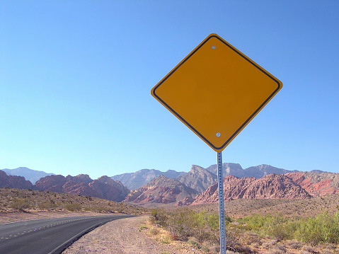 One way road transport sign with arrow on roadside or wayside, highway or freeway in California USA. Road trip in desert valley among mountains and hills with boulders. Western wilderness nature.