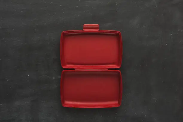 Red empty open plastic lunch box for food storage on black background with copy space, top view