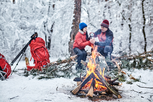 Happy couple  over a campfire in winter snowy forest