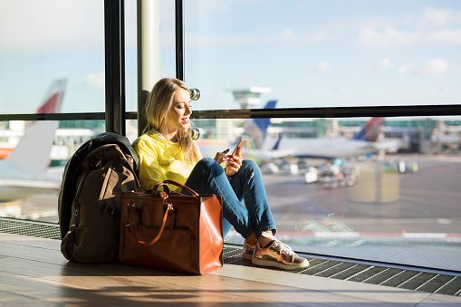 Woman sitting in airport and waiting for her flight, woman using phone in airport departure area