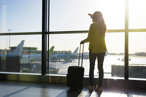 Silhouette of woman standing by window in airport, photo taken from back