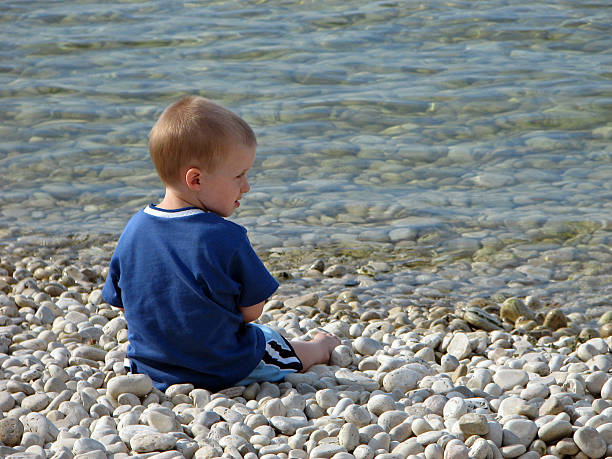 istock Young Boy Sitting on Rock Beach at Lake 91205620