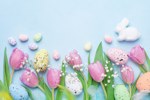 Spring background with flowers, bunny, colorful eggs and feathers on blue table top view. Happy Easter card. Copy space for text.