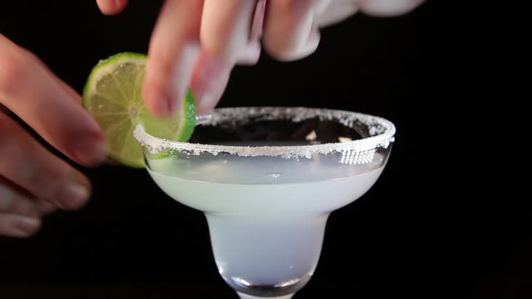 Process of serving margarita cocktail. Bartender pouring alcohol drink into a glass close-up