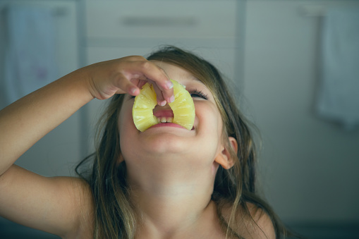 A happy pretty young girl is eating a slice of pineapple in a funny way.
