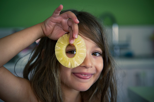 A young girl is peeking through the  hole of a pineapple slice. Funny, fresh, happy and humorous pose.