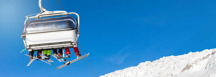 skiers and snowboarders in a ski lift against clear blue sky. blank space for text