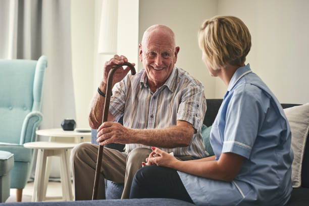 Smiling retired man with female home carer Smiling retired senior man sitting on sofa with female home carer at care home nursing home stock pictures, royalty-free photos & images