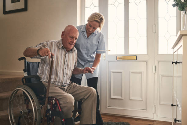 female carer helping disabled senior man to walk - wheelchair disabled senior adult female nurse imagens e fotografias de stock