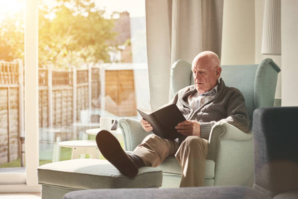 istock Senior man sitting on arm chair and reading a book 912073246