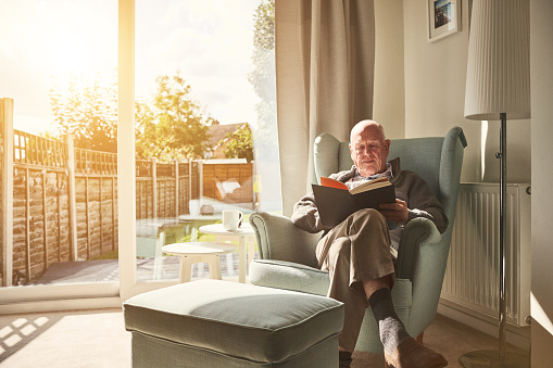 Indoor shot of mature man sitting on arm chair and reading a book at home