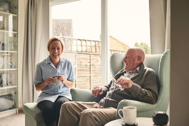 Senior man and female carer enjoying coffee at home Indoor shot of smiling senior man and female carer enjoying coffee in living room home carer stock pictures, royalty-free photos & images