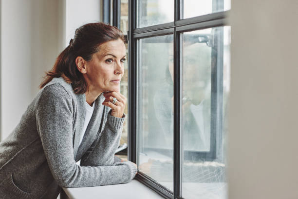 istock Thoughtful mature woman standing by the window 912082124