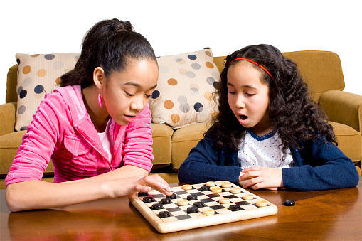 Two girls playing checkers. Girls are of Japanese, black and Briazilian background.