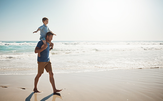 Shot of a father carrying his little son on his shoulders at the beach