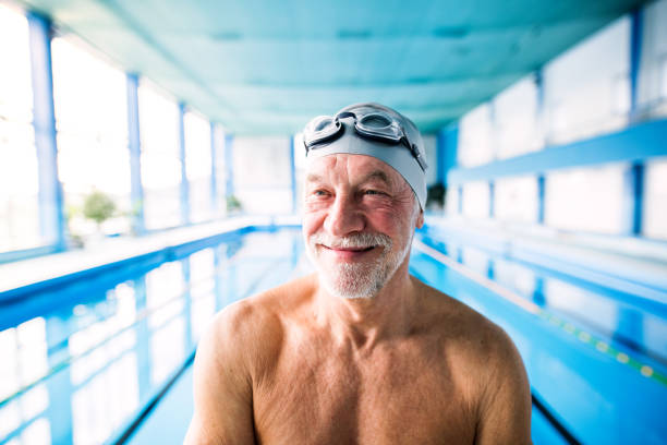 Senior man in an indoor swimming pool. Senior man in an indoor swimming pool. Active pensioner enjoying sport. swimming cap stock pictures, royalty-free photos & images