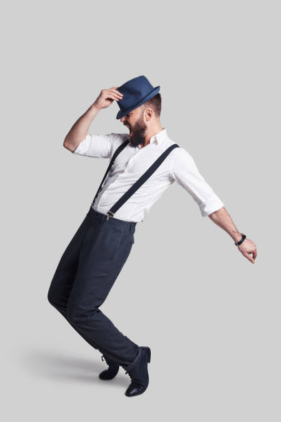 Perfect in every way. Full length of handsome young man in suspenders adjusting his hat and making a face while dancing against grey background vintage man suspenders stock pictures, royalty-free photos & images