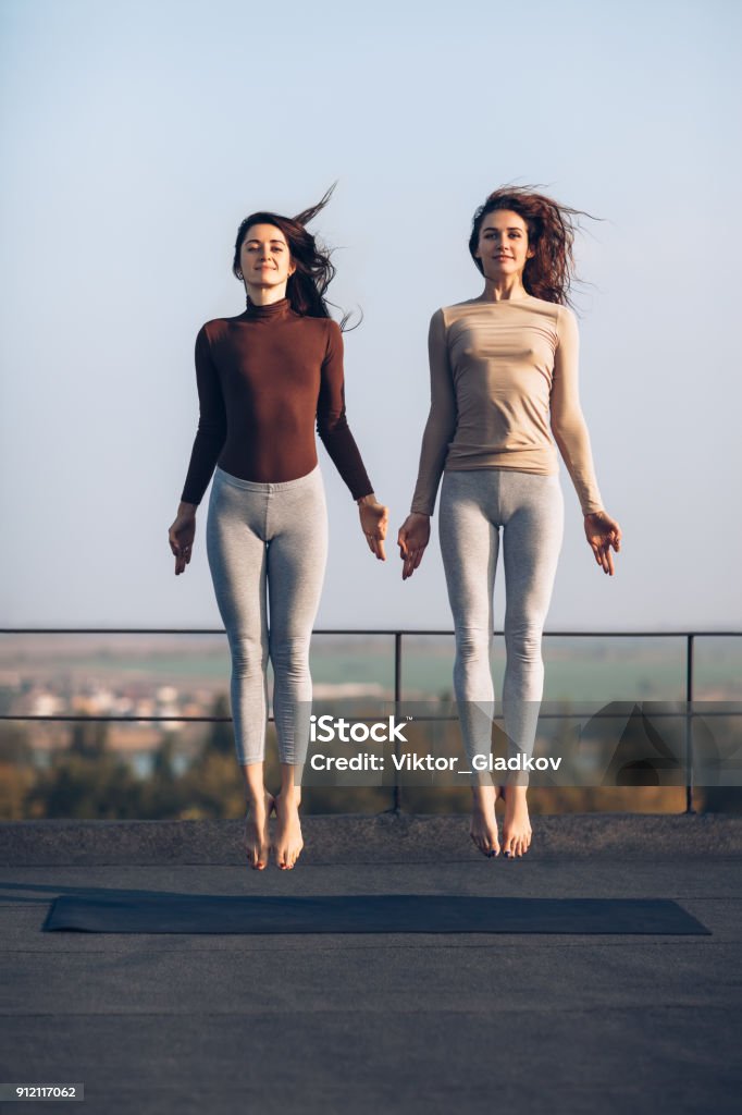 Deux belles jeunes femmes synchroniquement sautent sur le toit à l’extérieur - Photo de Femmes libre de droits