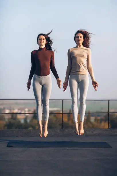 Photo of Two beautiful young women synchronously jump on the roof outdoors