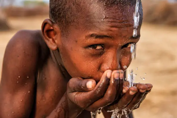 Photo of African young boy drinking fresh water on savanna, East Africa