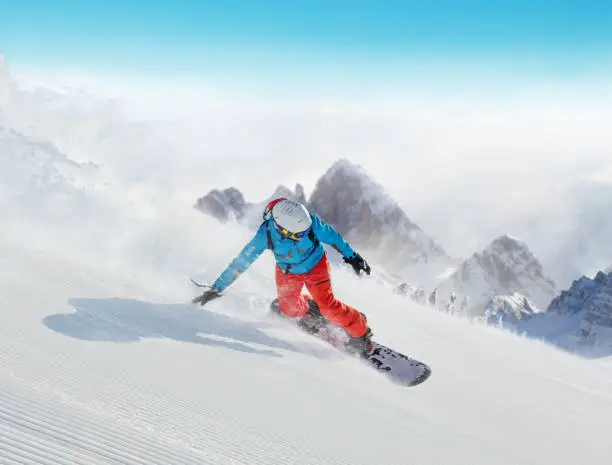 Young man snowboarder running downhill, Alpine mountains. Winter sport and recreation, leasure outdoor activities.