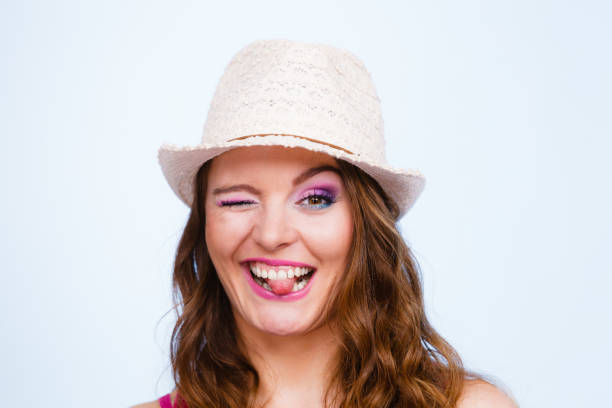 Woman face colorful eyes makeup summer straw hat on head smiling having fun closeup. Summer holidays and happiness, studio shot on blue