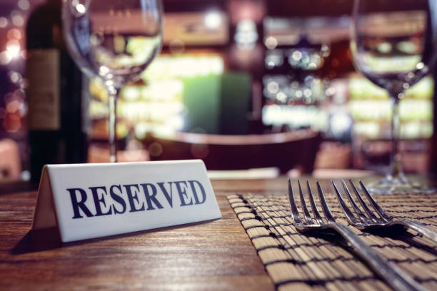 Reserved sign on restaurant table with bar background Restaurant reserved table sign with places setting and wine glasses ready for a party exclusive dinner stock pictures, royalty-free photos & images