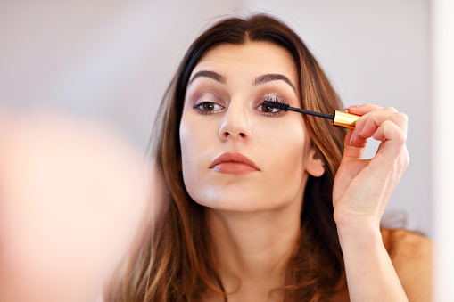 Mujer joven atractiva haciendo maquillaje mientras se mira en el espejo en el baño photo