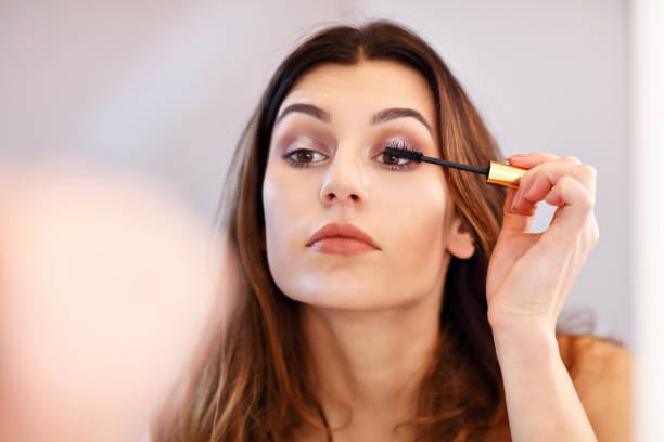 mujer joven atractiva haciendo maquillaje mientras se mira en el espejo en el baño - maquillaje fotografías e imágenes de stock