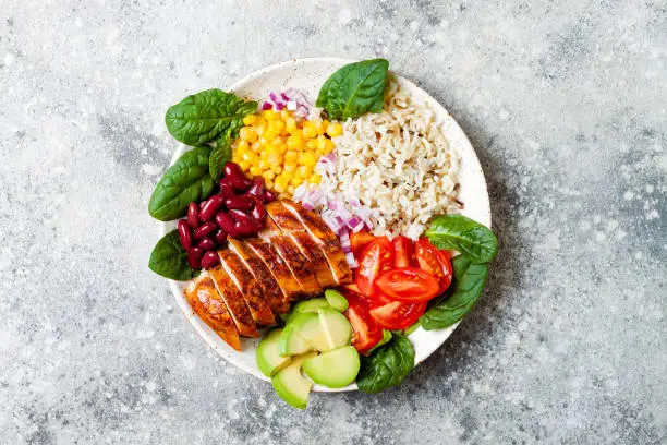 Photo of Homemade Mexican chicken burrito bowl with rice, beans, corn, tomato, avocado, spinach. Taco salad lunch bowl