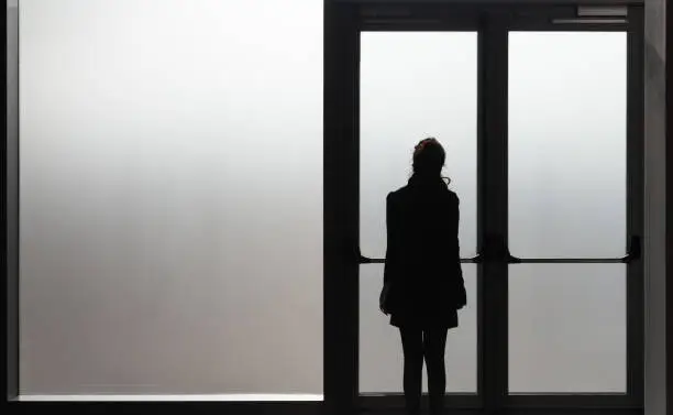 Photo of Depressed woman waiting in front a glass door in a white room ready to react - Disease - Abuse - phobia Concept