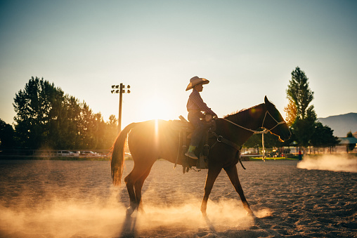 Little Boy horseback Riding in rodeo arena at sunrise