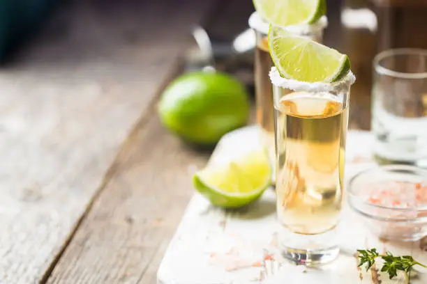 Mexican Gold Tequila shots with lime and salt on wooden table over black background