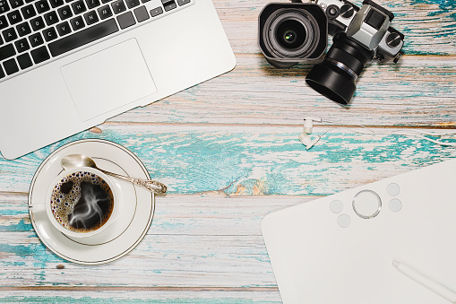 Vintage loft style wooden table with laptop, vintage camera with lenses, graphics tablet and a cup of coffee. Freelance photographer, blogger or designer workspace concept. Top view.