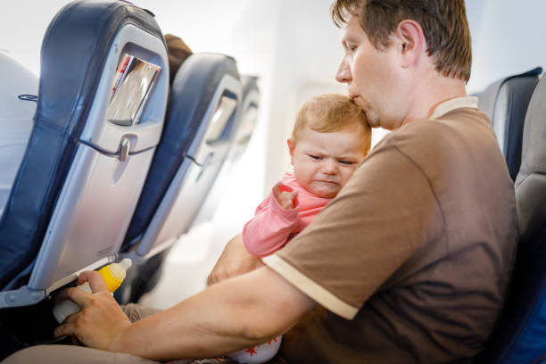 Young tired father and his crying baby daughter during flight on airplane going on vacations stock photo