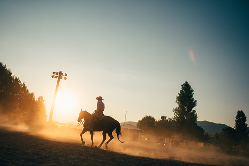 Cowboy Horseback riding in rodeo arena at sunrise