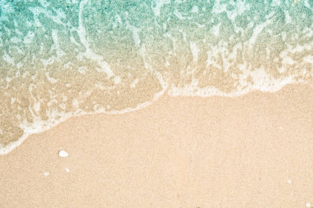 Photo of Soft wave of turquoise sea water on the sandy beach. Close-up and directly above photographed.