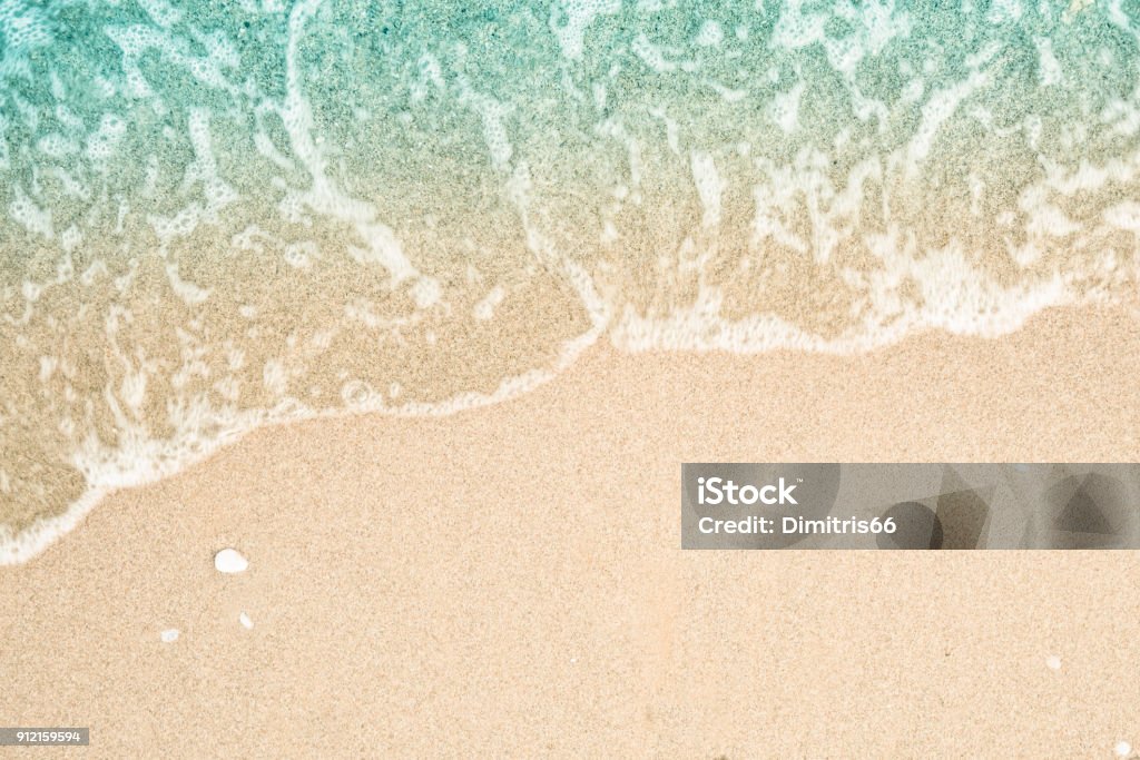 Soft wave of turquoise sea water on the sandy beach. Close-up and directly above photographed. Beach Stock Photo