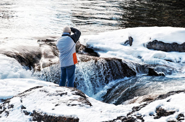 Bragg Creek, Aberta, Canada - December, 15, 2007: Rear view of a photographer taking pictures of the beautiful  landscape near the Elbow Falls in winter. The Elbow Falls are a popular tourist attraction  located near Bragg Creek in Kananaskis Country.
