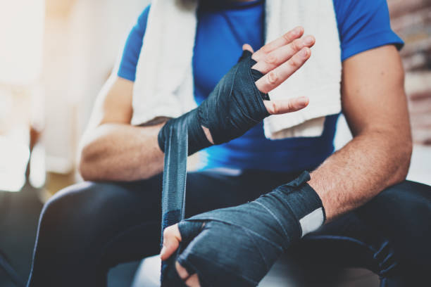 istock Muscular Boxer man prepairing hands for hard kickboxing training session in gym. Young athlete tying black boxing bandages.Blurred background. Horizontal. 912172074