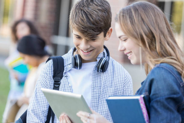 Male and female high school students look at something on social media while they wait for school to start. They are using a digital tablet.