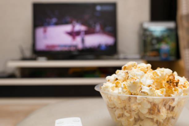 popcorn and remote control on sofa with a TV broadcasting basketball match on background stock photo