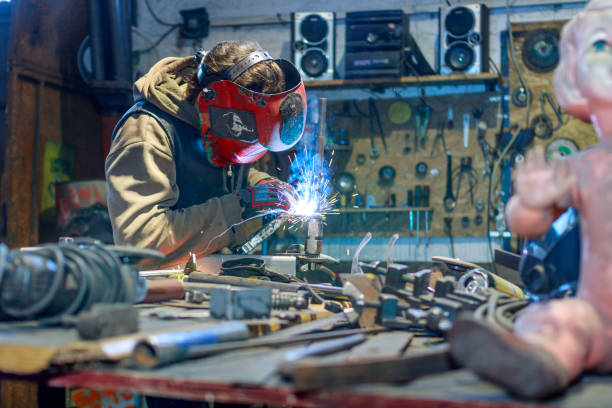 Young Artist worker at the Metal shop with the mask on his face welding in progress surrounded by tools and metal young man at the Metal shop with the mask on his face welding in progress surrounded by tools and metal welder engineering construction bright stock pictures, royalty-free photos & images