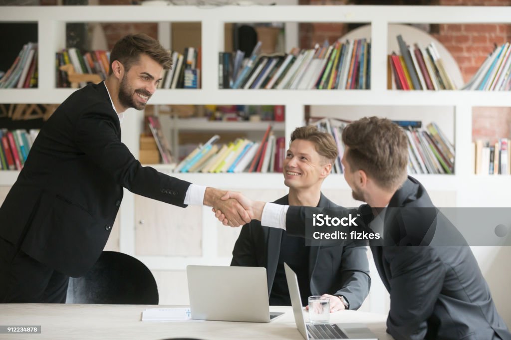 Businessman greeting welcoming new partner or making deal with handshake Businessman greeting congratulating new smiling executive team member or making deal with handshake at conference table, friendly company ceo shaking partners hand welcoming at meeting among three Beginnings Stock Photo