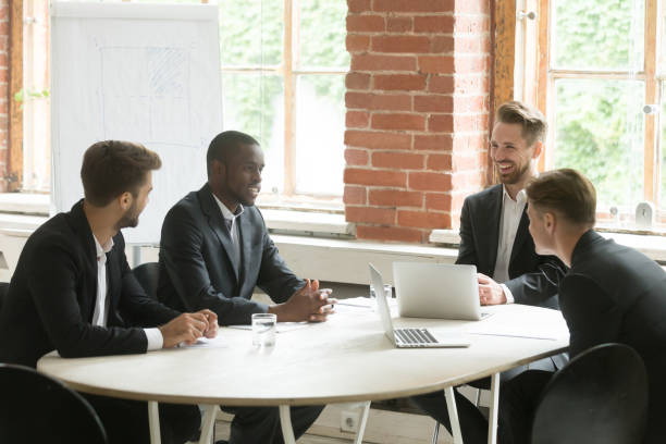istock Four satisfied smiling businessmen group talking laughing at meeting table 912234960