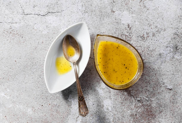 vinaigrette pour salade d’huile d’olive et de citron dans un plat de service et une cuillère d’argent sur une table en pierre - moutarde assaisonnements et vinaigrettes photos et images de collection