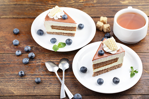 two pieces of cake with blueberries and tea stand on a wooden table