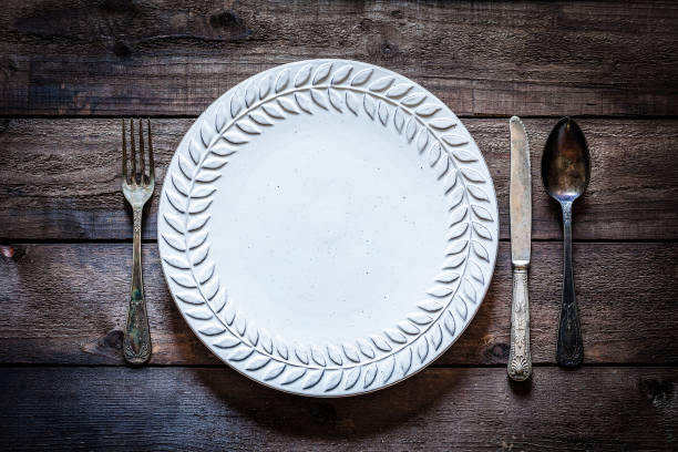 Vintage plate and silverware shot from above on rustic wooden table. The spoon and the knife are at the right of the plate and the fork is at the left. Predominant color is brown. Low key DSRL studio photo taken with Canon EOS 5D Mk II and Canon EF 100mm f/2.8L Macro IS USM