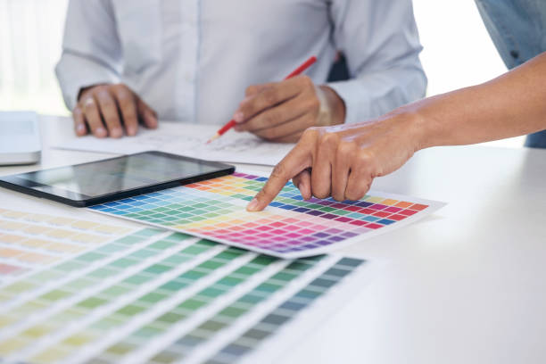 istock Two young interior design or graphic designer working on project of architecture drawing with work tools and color swatches, colour chart in digital tablet at workplace 912254728